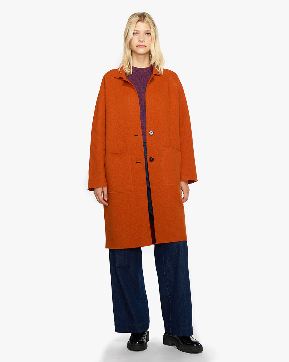 Oranges Wollmantel fuer Herbst. Der Übergangsmantel besticht durch eine lockere Oversize-Silhouette mit aufgesetzten Taschen, Raglanärmeln und Knopfverschluss.