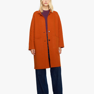 Oranges Wollmantel fuer Herbst. Der Übergangsmantel besticht durch eine lockere Oversize-Silhouette mit aufgesetzten Taschen, Raglanärmeln und Knopfverschluss.